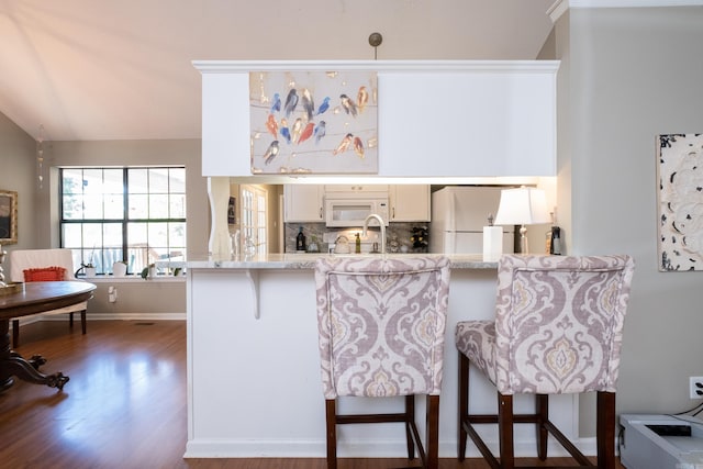 kitchen featuring white appliances, kitchen peninsula, and a breakfast bar area