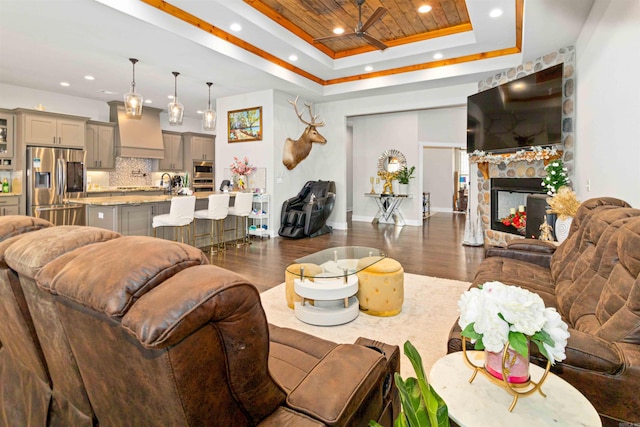 living room with a stone fireplace, a raised ceiling, sink, dark hardwood / wood-style floors, and wood ceiling