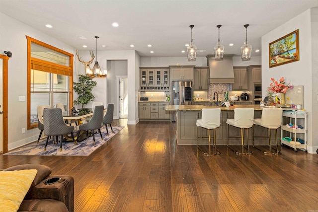 kitchen featuring pendant lighting, custom exhaust hood, a kitchen breakfast bar, gray cabinets, and appliances with stainless steel finishes