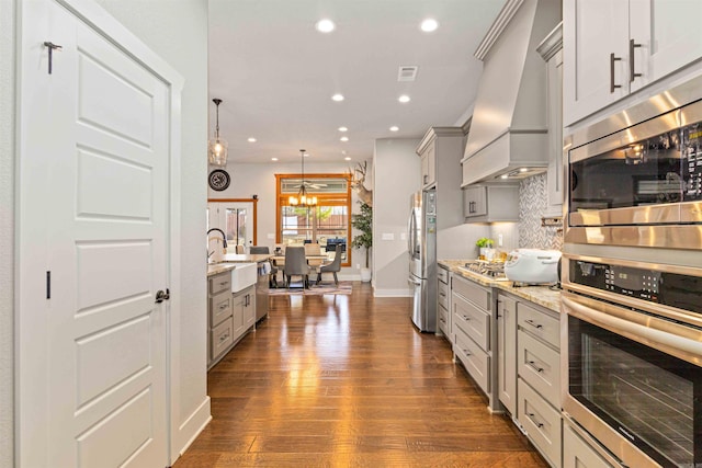 kitchen with pendant lighting, custom exhaust hood, decorative backsplash, light stone countertops, and stainless steel appliances