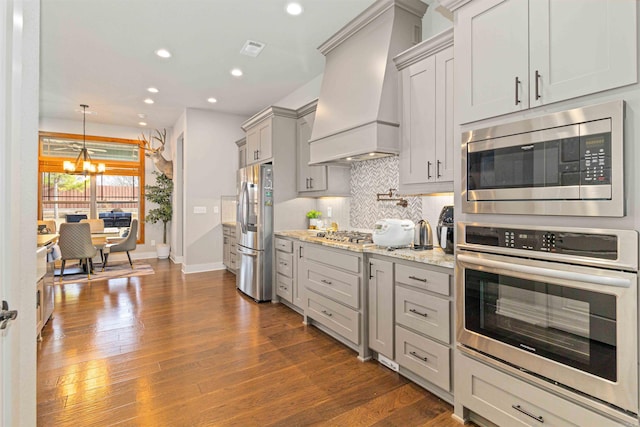 kitchen featuring light stone countertops, dark hardwood / wood-style flooring, a chandelier, appliances with stainless steel finishes, and custom exhaust hood