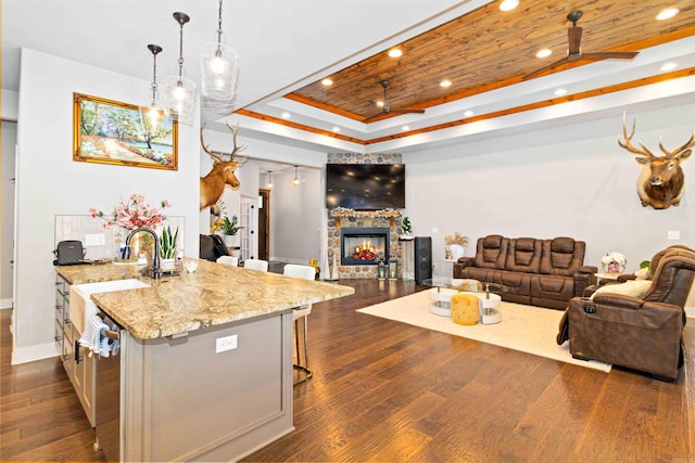 kitchen featuring ceiling fan, sink, a kitchen breakfast bar, light stone counters, and decorative light fixtures