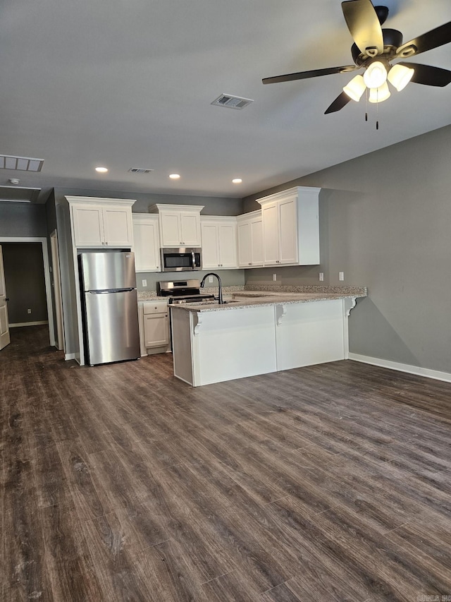 kitchen with dark wood-type flooring, white cabinets, ceiling fan, a kitchen bar, and stainless steel appliances