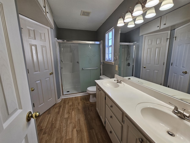 bathroom with wood-type flooring, a textured ceiling, toilet, vanity, and a shower with shower door