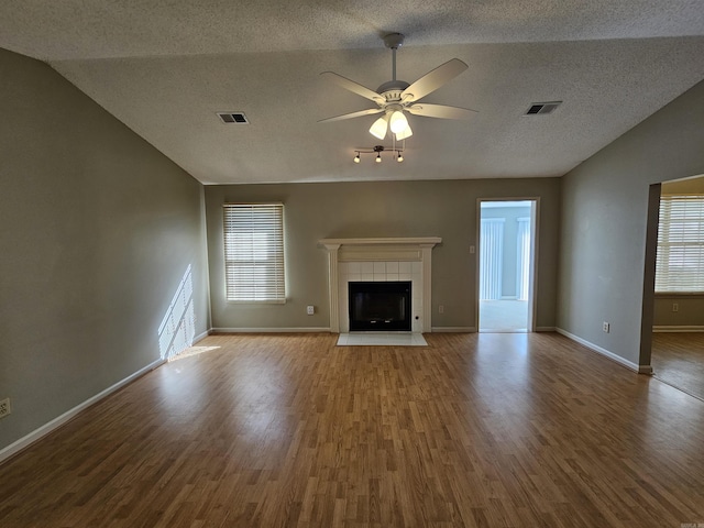 unfurnished living room featuring a tiled fireplace, a wealth of natural light, lofted ceiling, and hardwood / wood-style flooring