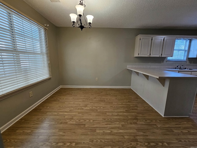 unfurnished dining area featuring sink, a textured ceiling, dark wood-type flooring, and a notable chandelier