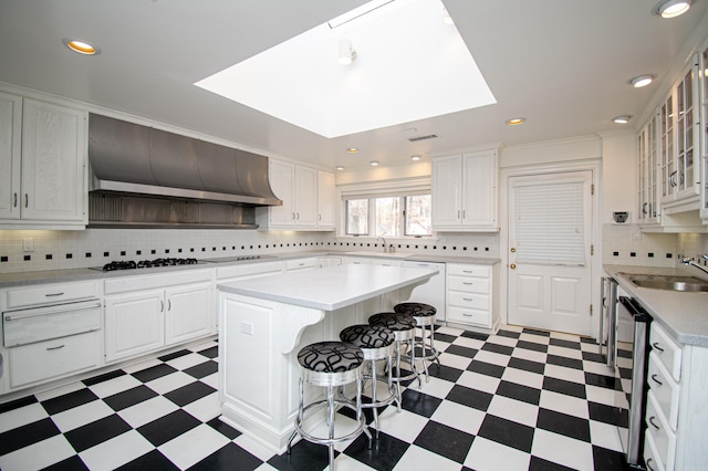 kitchen with white cabinets, wall chimney range hood, a skylight, a kitchen island, and stainless steel appliances