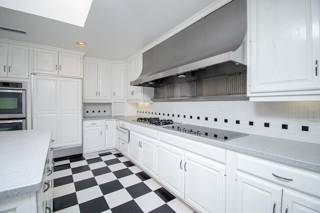 kitchen with tasteful backsplash, white cabinets, wall chimney exhaust hood, and appliances with stainless steel finishes