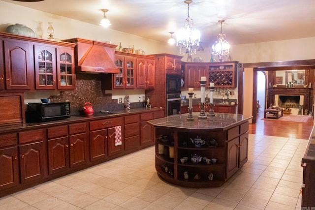 kitchen with an inviting chandelier, backsplash, a kitchen island, black appliances, and custom range hood