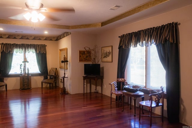 living area with hardwood / wood-style flooring, ceiling fan, and a tray ceiling