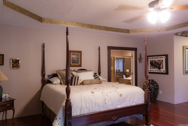 bedroom with a raised ceiling, connected bathroom, ceiling fan, and wood-type flooring