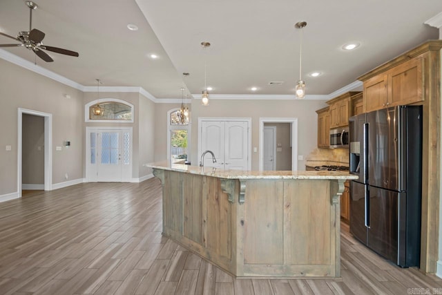 kitchen with light stone countertops, stainless steel appliances, decorative light fixtures, light hardwood / wood-style floors, and a large island