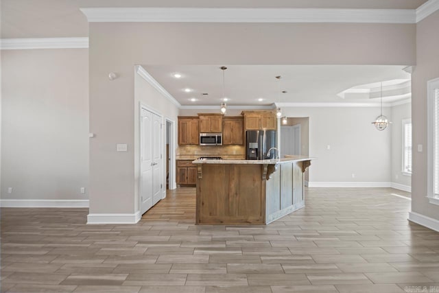 kitchen featuring pendant lighting, a breakfast bar, a center island with sink, crown molding, and appliances with stainless steel finishes