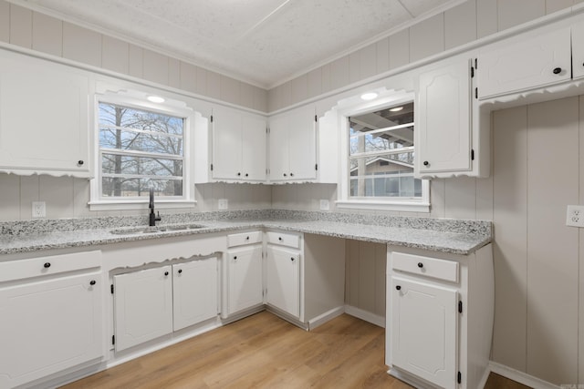 kitchen with crown molding, sink, light wood-type flooring, light stone counters, and white cabinetry