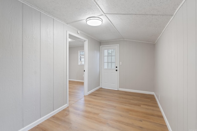 foyer featuring crown molding, wooden walls, and light wood-type flooring