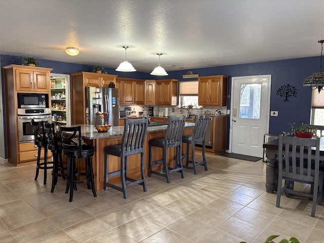 kitchen with dark stone countertops, pendant lighting, a kitchen island, and stainless steel appliances