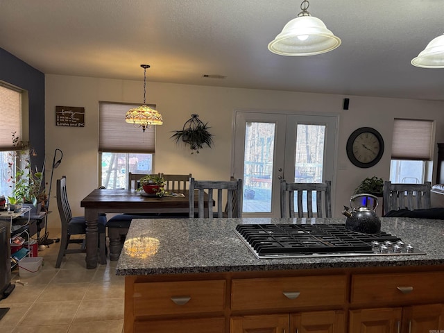 kitchen with french doors, pendant lighting, dark stone countertops, stainless steel gas stovetop, and light tile patterned flooring