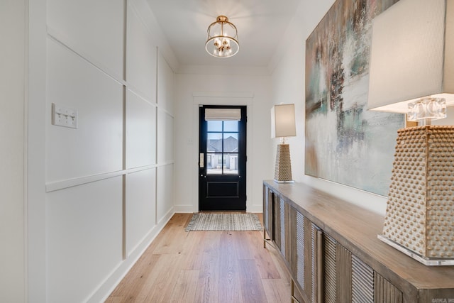 doorway to outside featuring crown molding, a chandelier, and light wood-type flooring