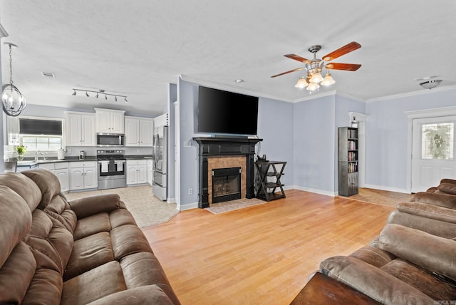 living room featuring ornamental molding, ceiling fan, sink, a tile fireplace, and light hardwood / wood-style flooring