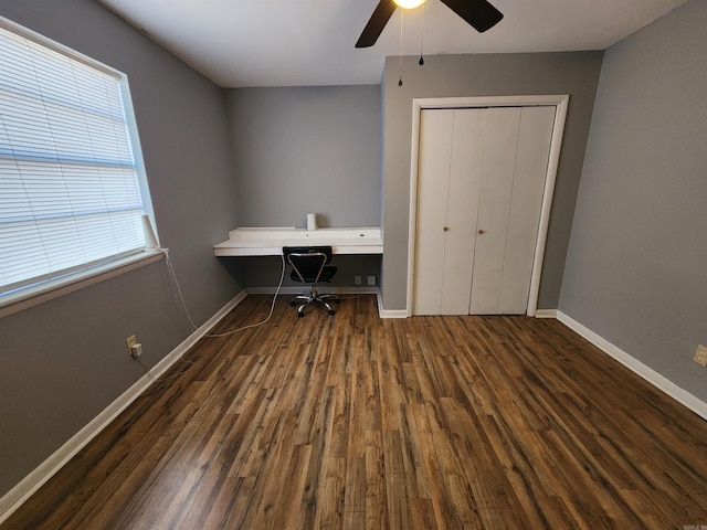 unfurnished office featuring ceiling fan, built in desk, and dark hardwood / wood-style floors