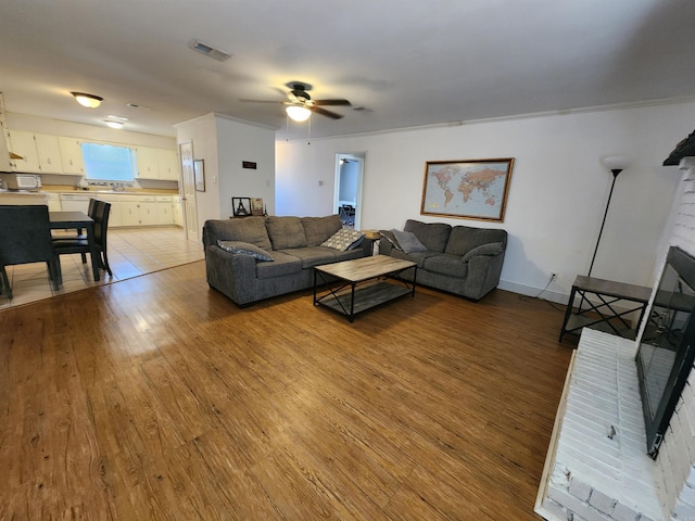 living room featuring a fireplace, ceiling fan, light hardwood / wood-style flooring, and ornamental molding