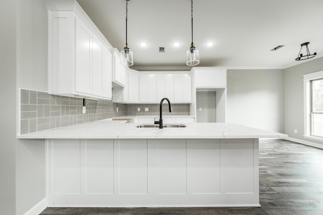 kitchen with kitchen peninsula, light stone countertops, sink, pendant lighting, and white cabinets