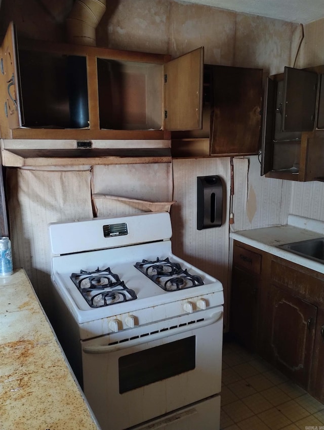 kitchen with light tile patterned floors, white gas range oven, and dark brown cabinetry