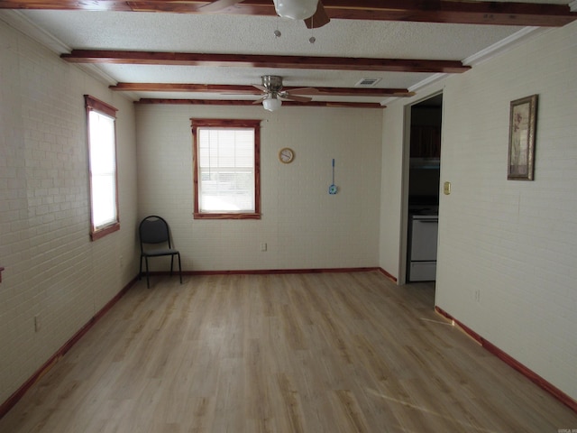 unfurnished room with ceiling fan, light wood-type flooring, a textured ceiling, beamed ceiling, and brick wall