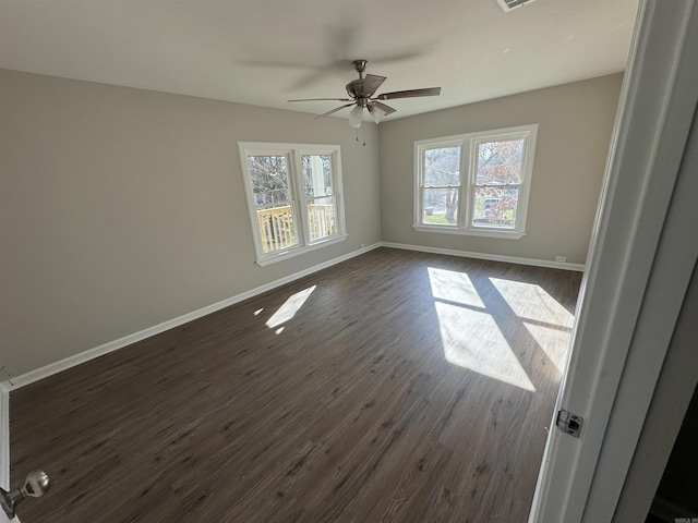 empty room featuring plenty of natural light, ceiling fan, and dark wood-type flooring