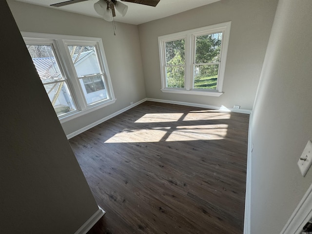 empty room with a healthy amount of sunlight, ceiling fan, and dark wood-type flooring