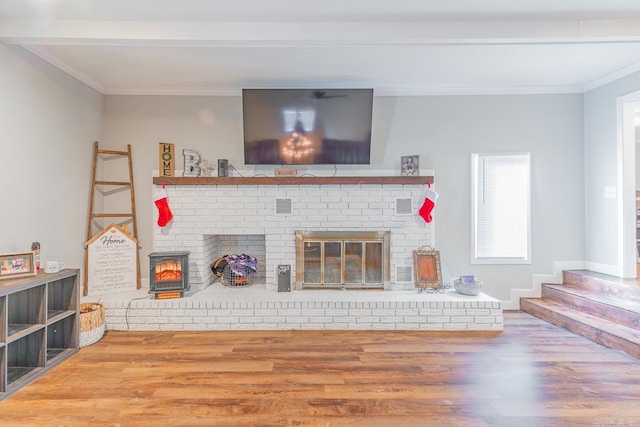 living room featuring beamed ceiling, wood-type flooring, crown molding, and a brick fireplace