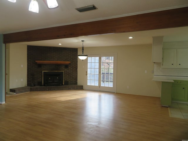 unfurnished living room featuring beam ceiling, a brick fireplace, and light wood-type flooring