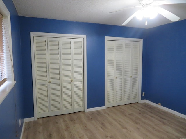 unfurnished bedroom featuring ceiling fan, light hardwood / wood-style floors, a textured ceiling, and two closets