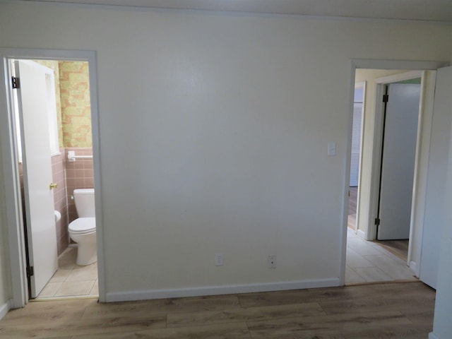 interior space with connected bathroom, light hardwood / wood-style floors, and tile walls