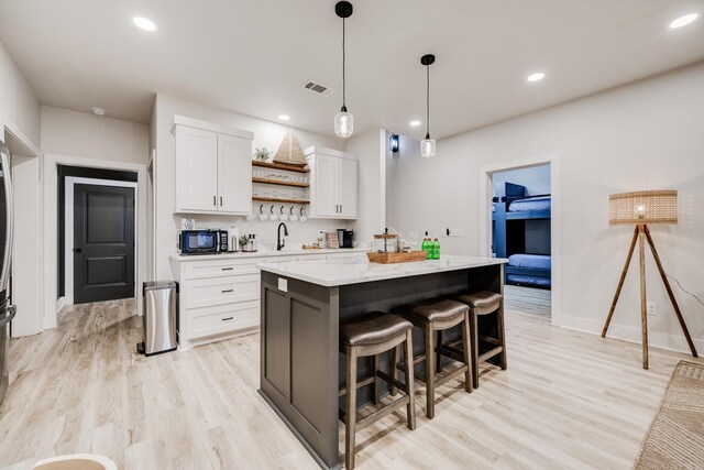 kitchen featuring white cabinetry, sink, hanging light fixtures, light hardwood / wood-style floors, and a kitchen island