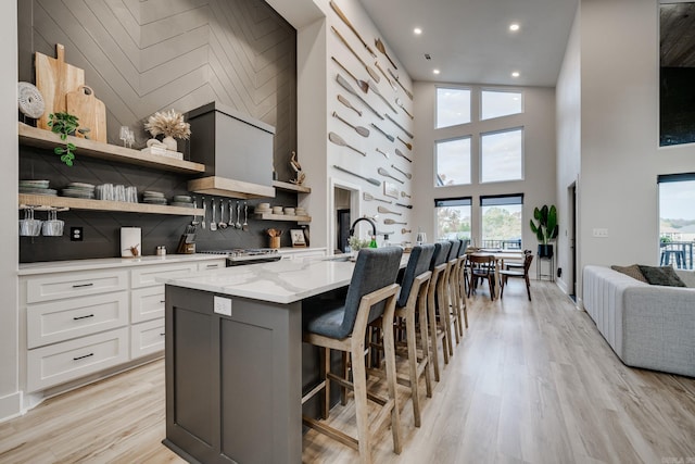 kitchen with white cabinetry, a high ceiling, light stone counters, light hardwood / wood-style flooring, and a kitchen island with sink