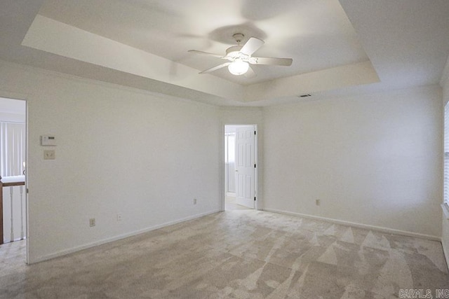 empty room with ceiling fan, light colored carpet, and a tray ceiling