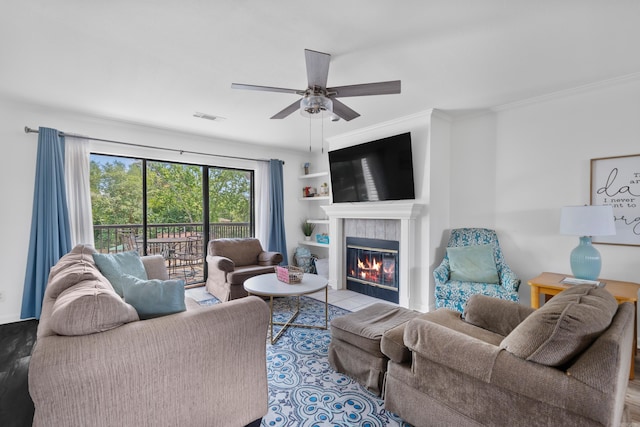 living room featuring a tiled fireplace, ceiling fan, built in features, and crown molding