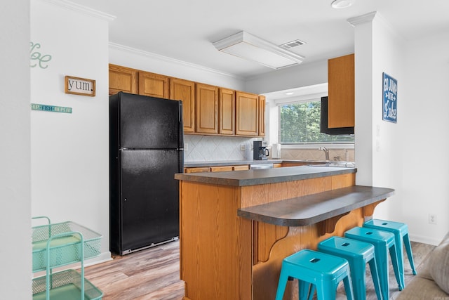 kitchen featuring black refrigerator, a kitchen bar, light wood-type flooring, kitchen peninsula, and sink