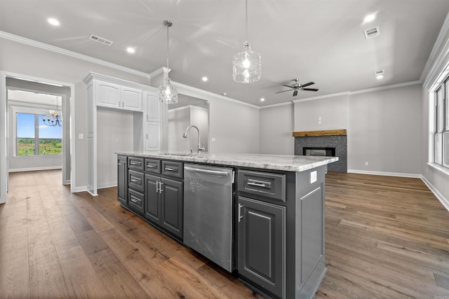 kitchen with stainless steel dishwasher, ceiling fan with notable chandelier, a fireplace, white cabinetry, and an island with sink