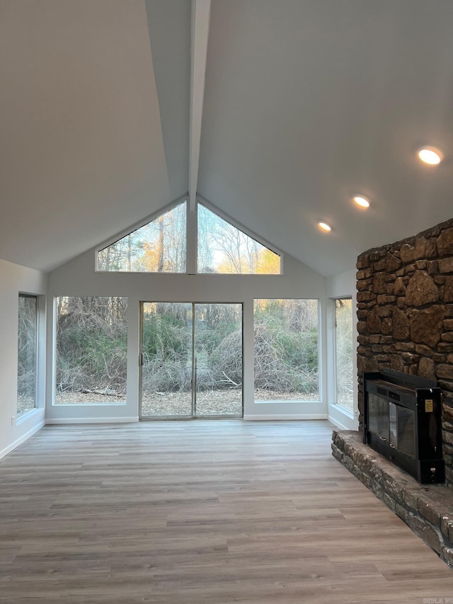 unfurnished living room with lofted ceiling with beams, light hardwood / wood-style floors, a stone fireplace, and a wealth of natural light