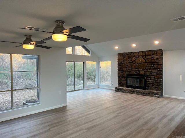 unfurnished living room with ceiling fan, a stone fireplace, lofted ceiling, and light wood-type flooring