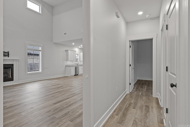 hall with light hardwood / wood-style flooring, a towering ceiling, and sink