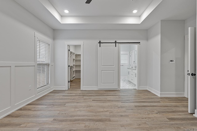 unfurnished bedroom featuring a barn door, light wood-type flooring, a spacious closet, and connected bathroom