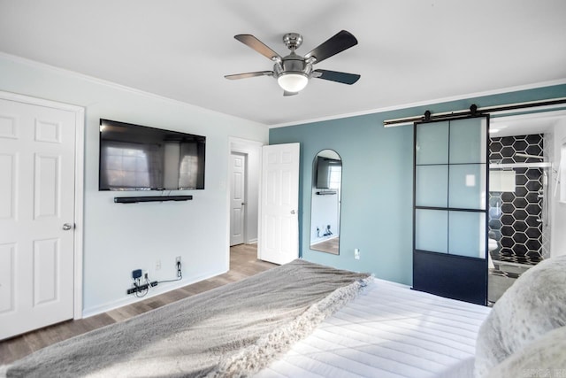 unfurnished bedroom with hardwood / wood-style flooring, ceiling fan, a barn door, and ornamental molding