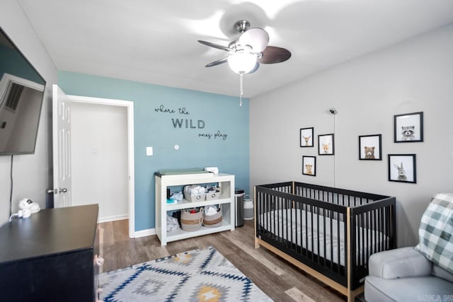 bedroom with a crib, dark hardwood / wood-style floors, and ceiling fan