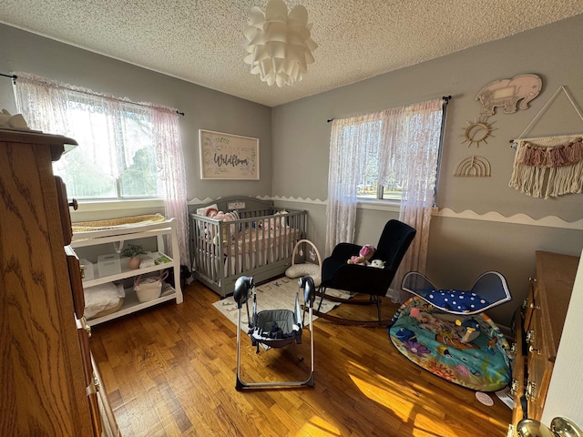 bedroom with a textured ceiling, multiple windows, a nursery area, and wood finished floors