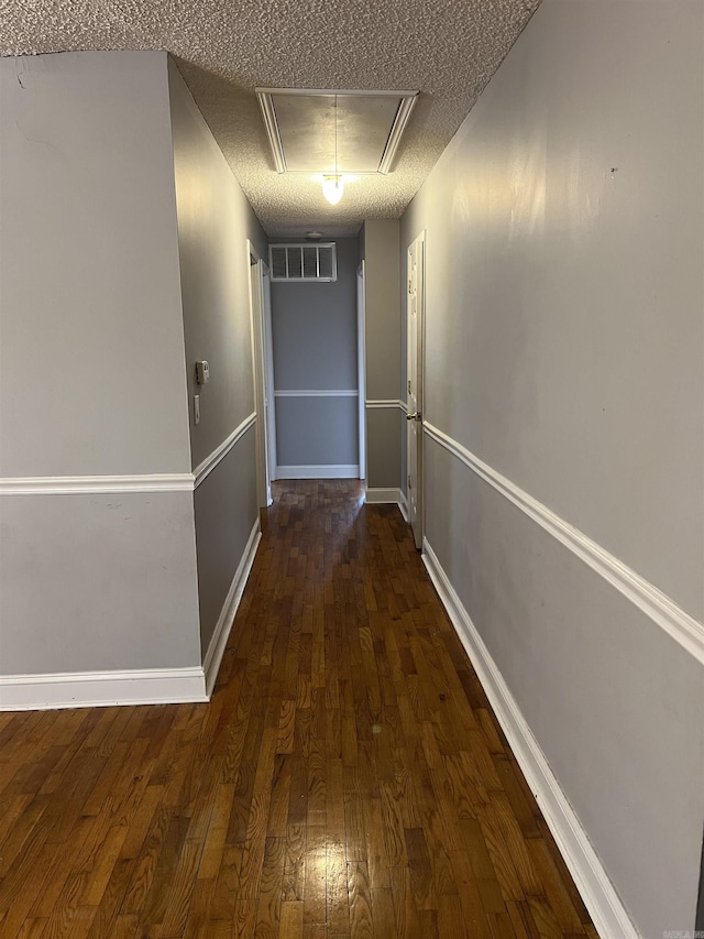 corridor with attic access, baseboards, visible vents, dark wood-type flooring, and a textured ceiling