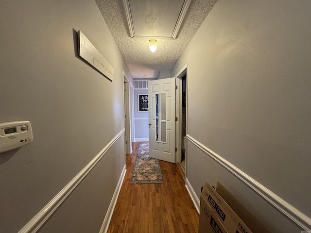 hallway featuring a textured ceiling, wood finished floors, visible vents, and baseboards