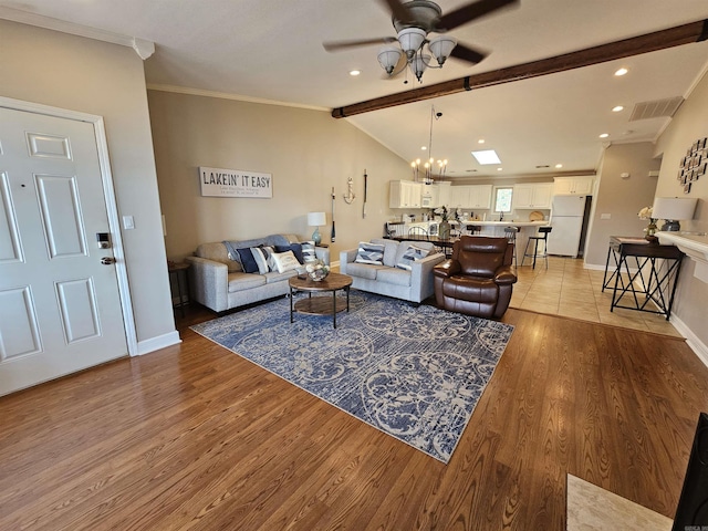 living room featuring vaulted ceiling with skylight, ceiling fan with notable chandelier, light wood-type flooring, and crown molding